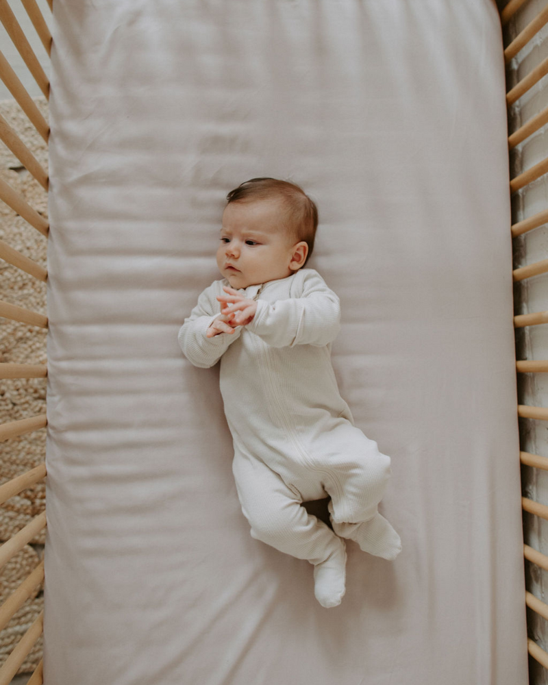 Bébé dans un lit avec literie couleur pivoine.