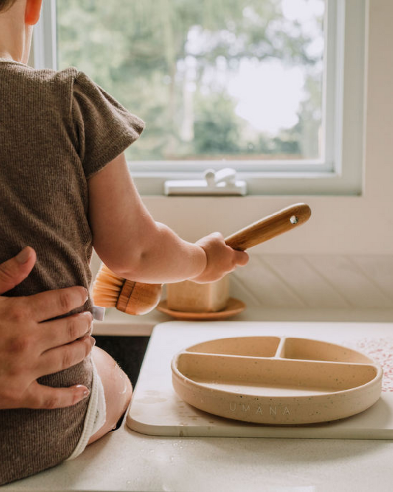 Enfant qui joue avec vaisselle en silicone couleur maïs.