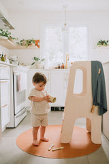 Enfant qui joue debout sur un tapis de cuir végan rond côté tan.