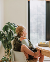 Enfant mangeant à table avec bavette en silicone couleur grège.